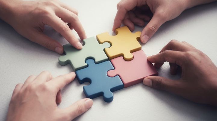 Four hands fitting puzzle pieces together